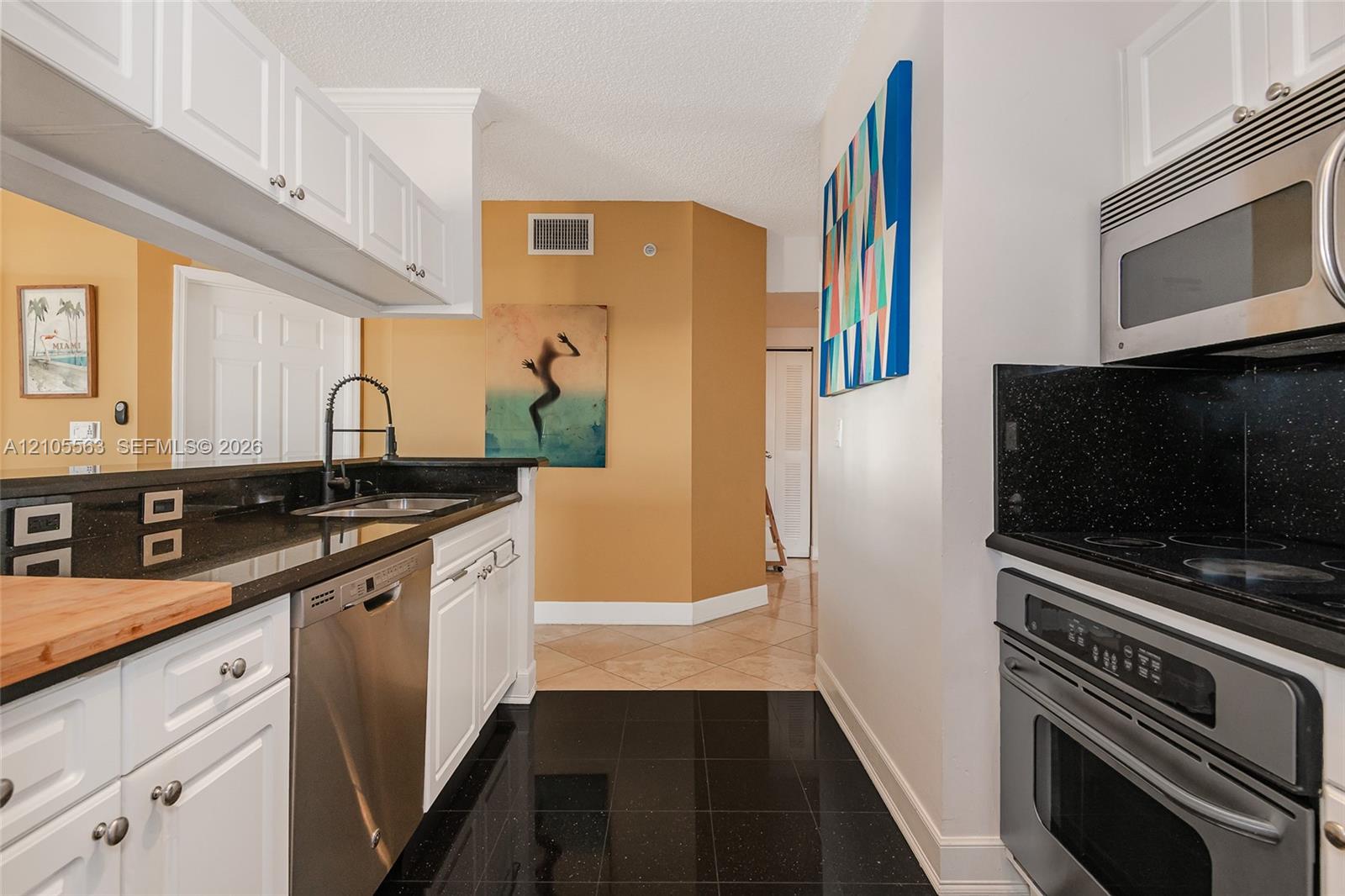 White shaker-style cabinetry with stainless steel appliances, black countertops, and a black pull-down faucet