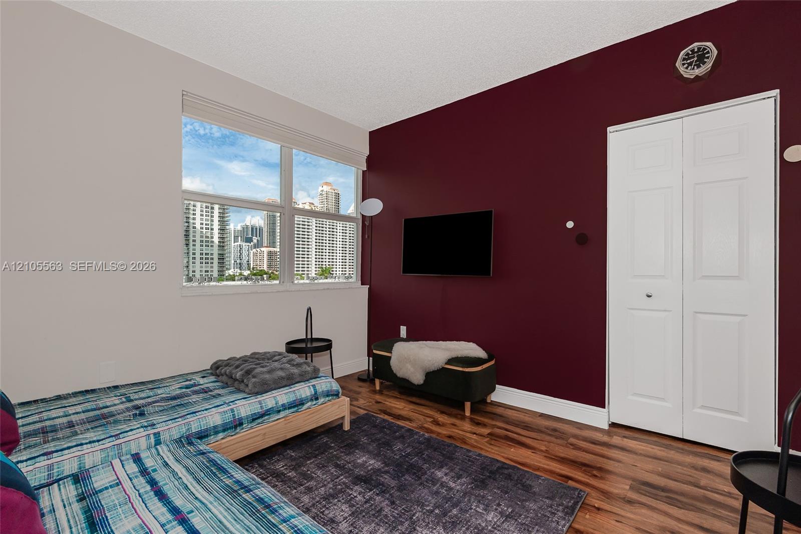Expansive window with urban building scenery, wood-finish flooring, two-panel bifold closet doors, and a wall-mounted television