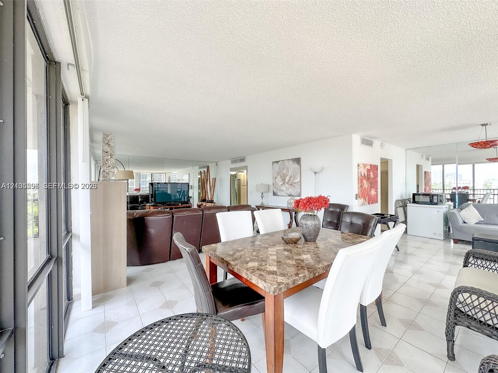 Open living area featuring large-format ceramic tile flooring, expansive floor-to-ceiling glass sliding doors, and wall-to-wall mirror paneling