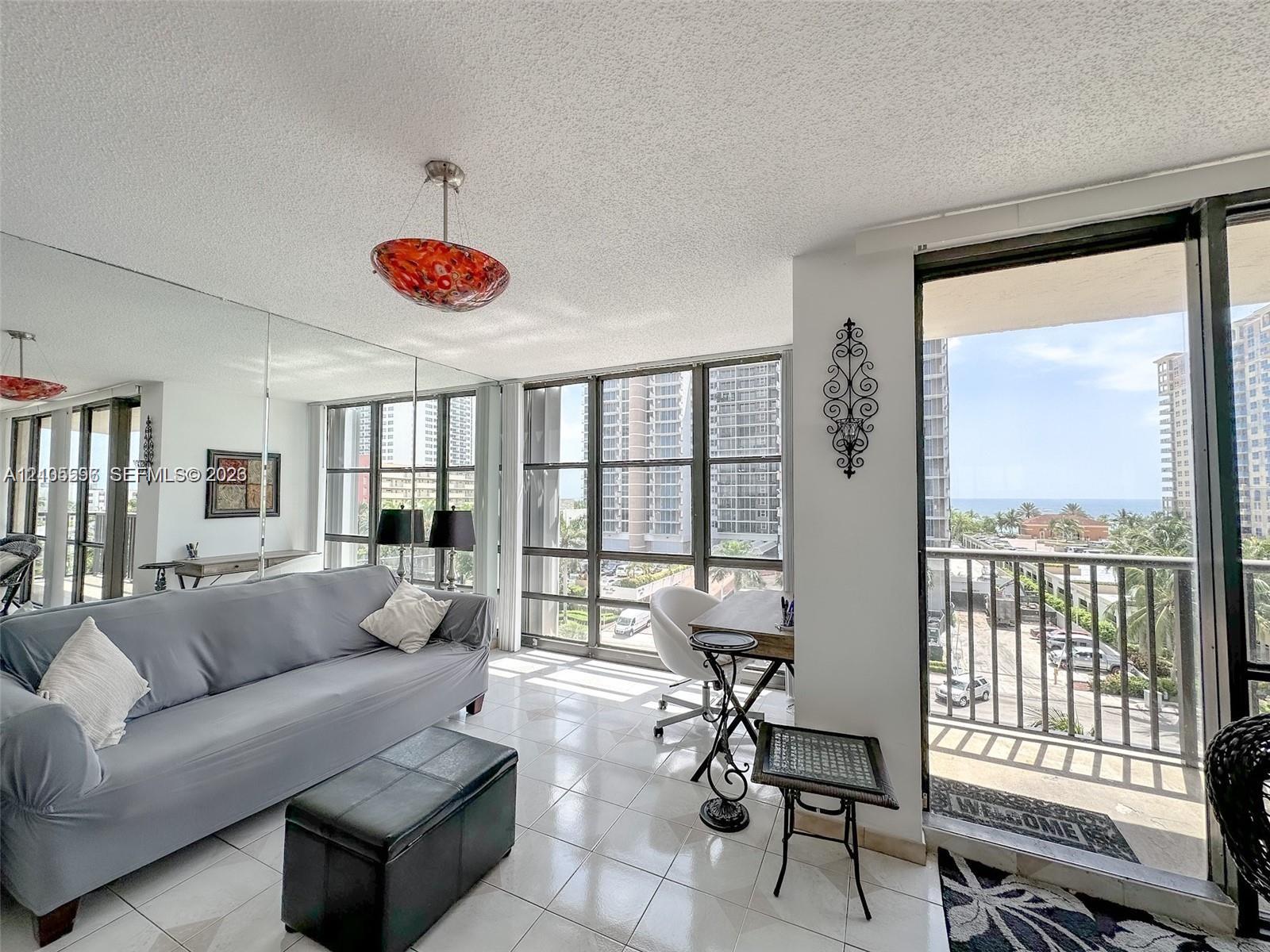 Floor-to-ceiling windows, mirrored accent wall, light-toned tile flooring, and a private balcony