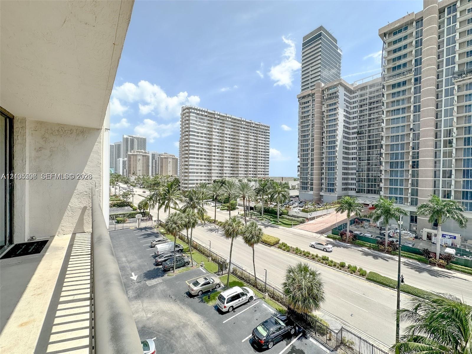 Elevated balcony featuring a metal railing and concrete flooring with an urban perspective of multi-story architecture and mature palm trees