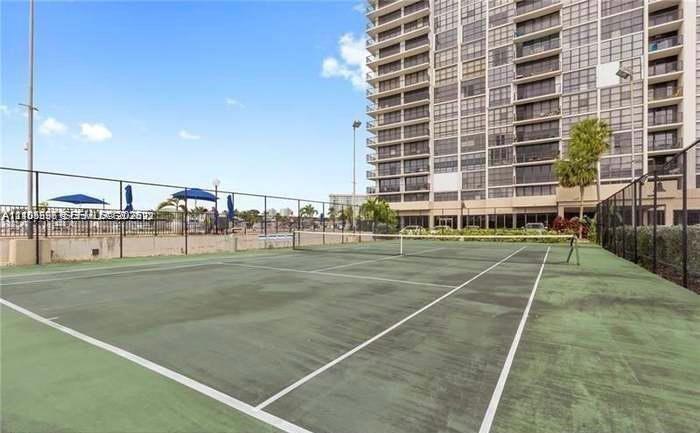 Outdoor tennis court with green surface and perimeter fencing