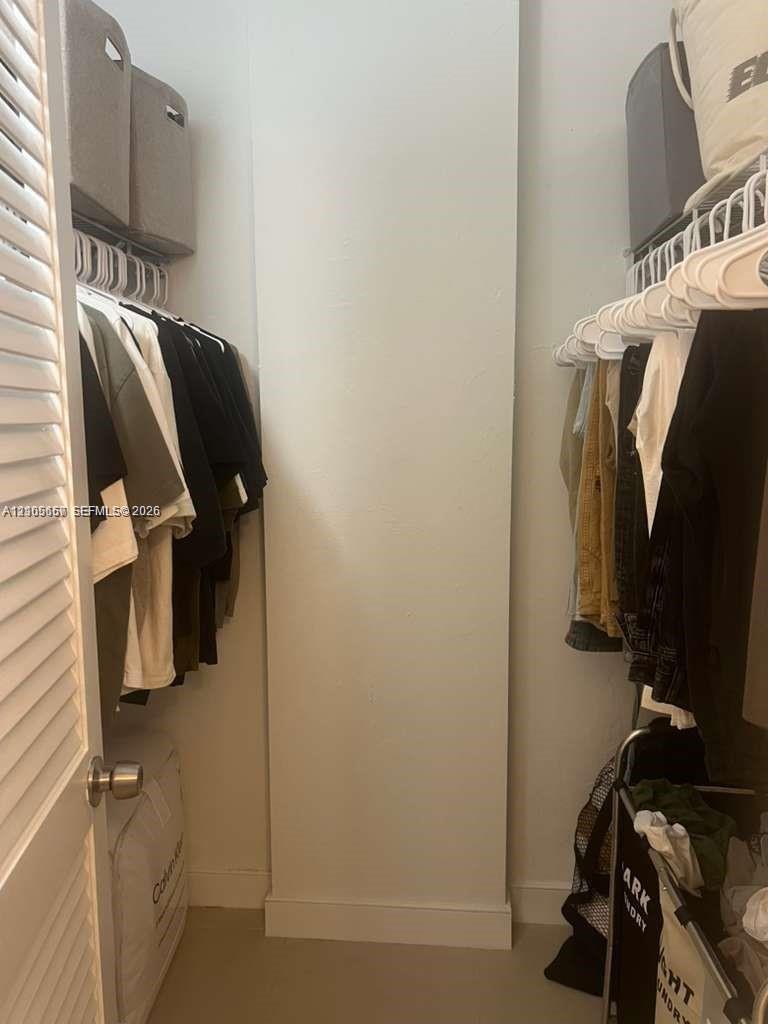 Walk-in closet featuring built-in white wire shelving, overhead storage compartments, and a white louvered door
