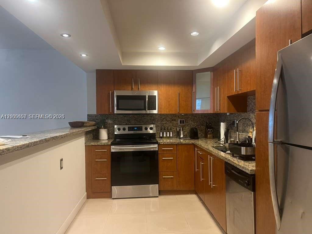 Kitchen featuring wood cabinetry, stone countertops, stainless steel appliances, recessed ceiling lighting, and a breakfast bar