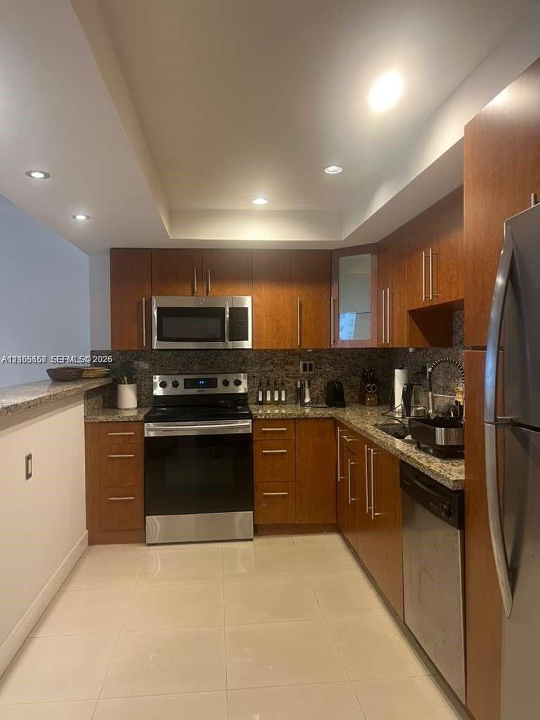 Kitchen featuring wood cabinetry, stone-surface countertops, stainless steel appliances, recessed ceiling lighting, and tile flooring
