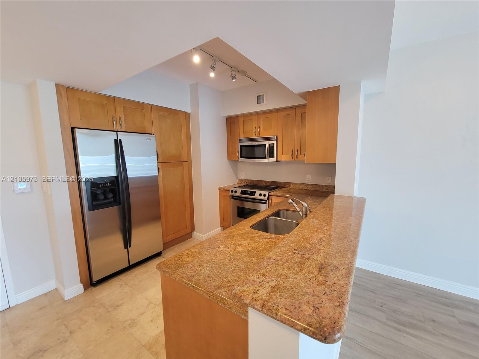 Kitchen featuring natural wood cabinetry, stone countertops, stainless steel appliances, a double-basin undermount sink, and recessed track lighting