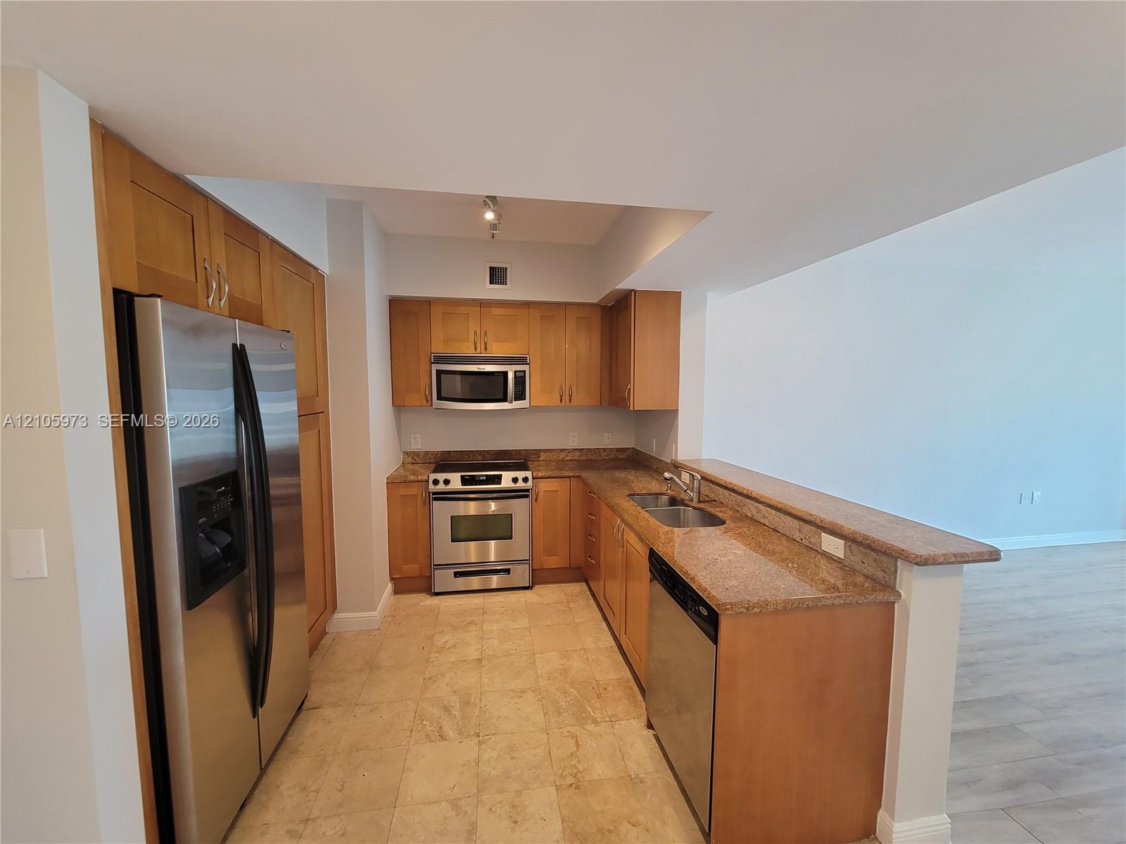 Kitchen featuring natural wood cabinetry, stone countertops, stainless steel appliances, a double-basin undermount sink, and tiled flooring