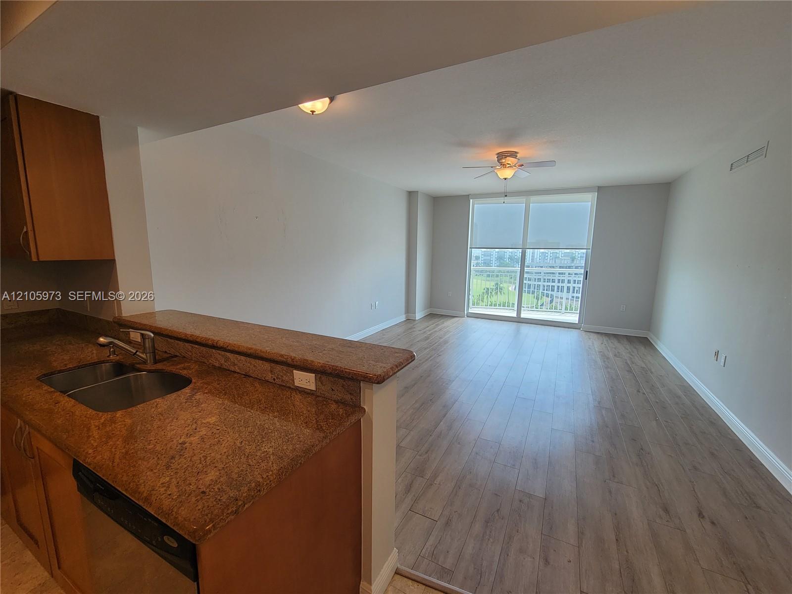 Kitchen featuring a breakfast bar, stone-surface countertops, dual-basin stainless steel sink, and wood-finish flooring extending into the main area with floor-to-ceiling glass sliding doors