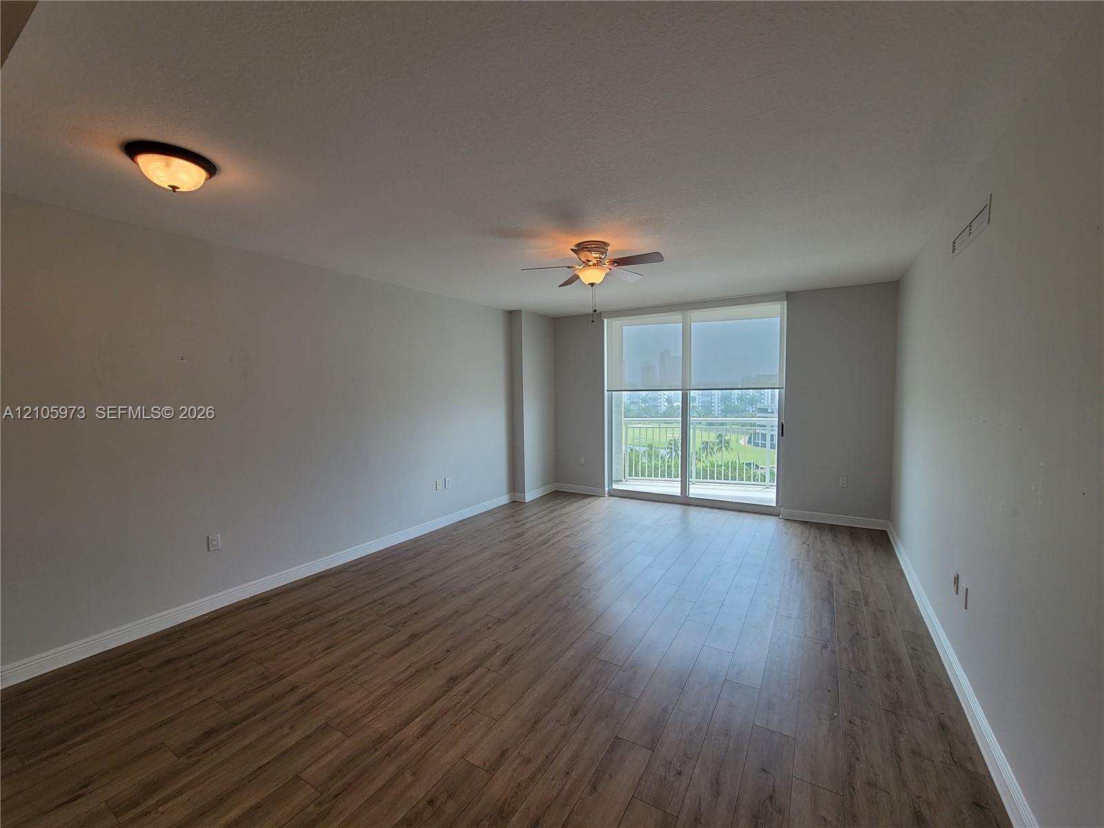 Open-concept room featuring wood-finish flooring, ceiling fan, flush-mount lighting, and large sliding glass door with access to a balcony