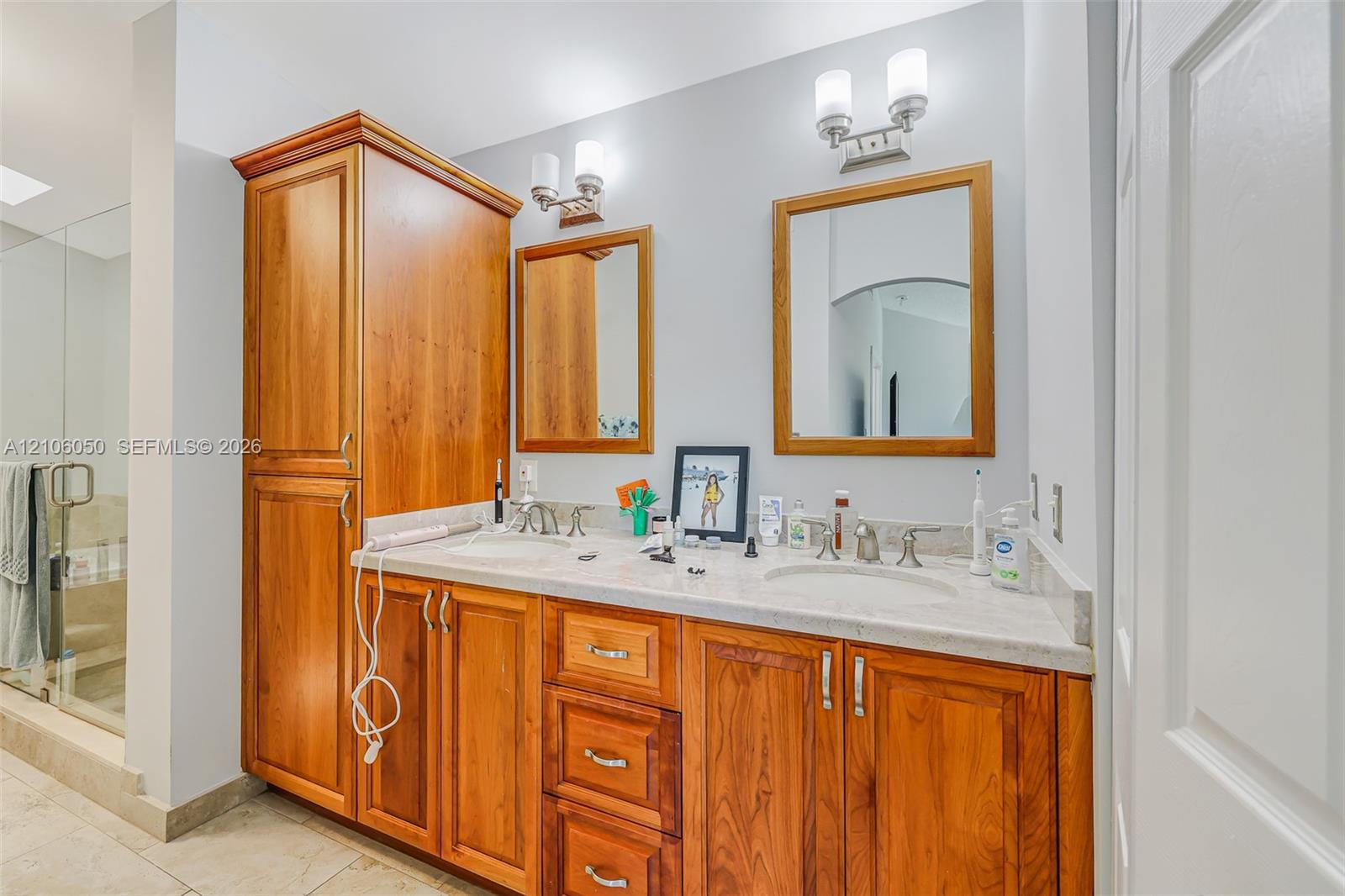 Dual-sink vanity with natural wood cabinetry, stone countertop, matching wood-framed mirrors, and brushed metal wall-mounted lighting