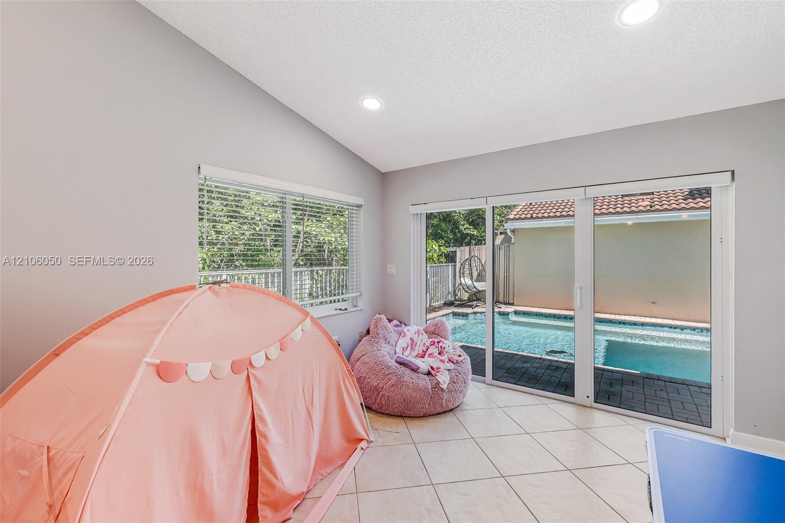 Vaulted ceiling featuring recessed lighting, large-format tile flooring, and sliding glass doors opening to an exterior swimming pool