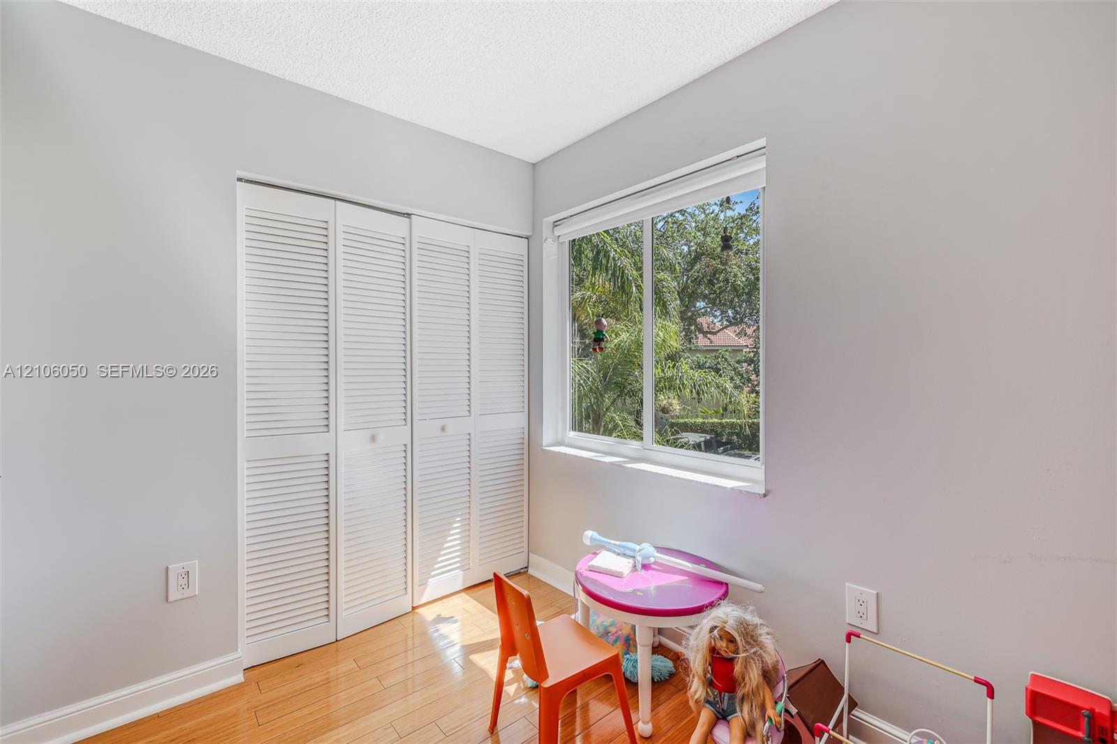 Bedroom featuring wood-finish flooring, a double-panel louvered closet, and a large horizontal window providing exterior greenery