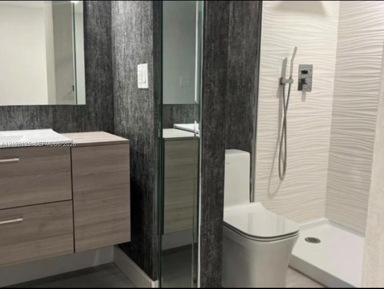 Modern floating vanity with wood-finish cabinetry, white textured wave-patterned shower wall tiling, floor-to-ceiling mirror panel, and wall-mounted hand shower fixture
