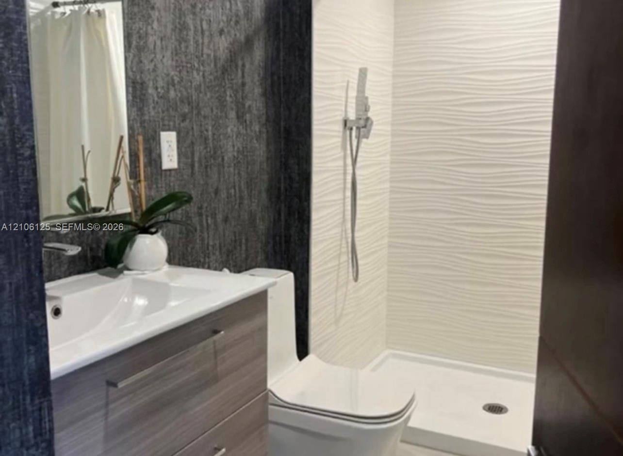 Bathroom featuring a floating vanity with a integrated sink, textured charcoal wall surfacing, a walk-in shower with white wavy-pattern tile, and a wall-mounted handheld shower fixture