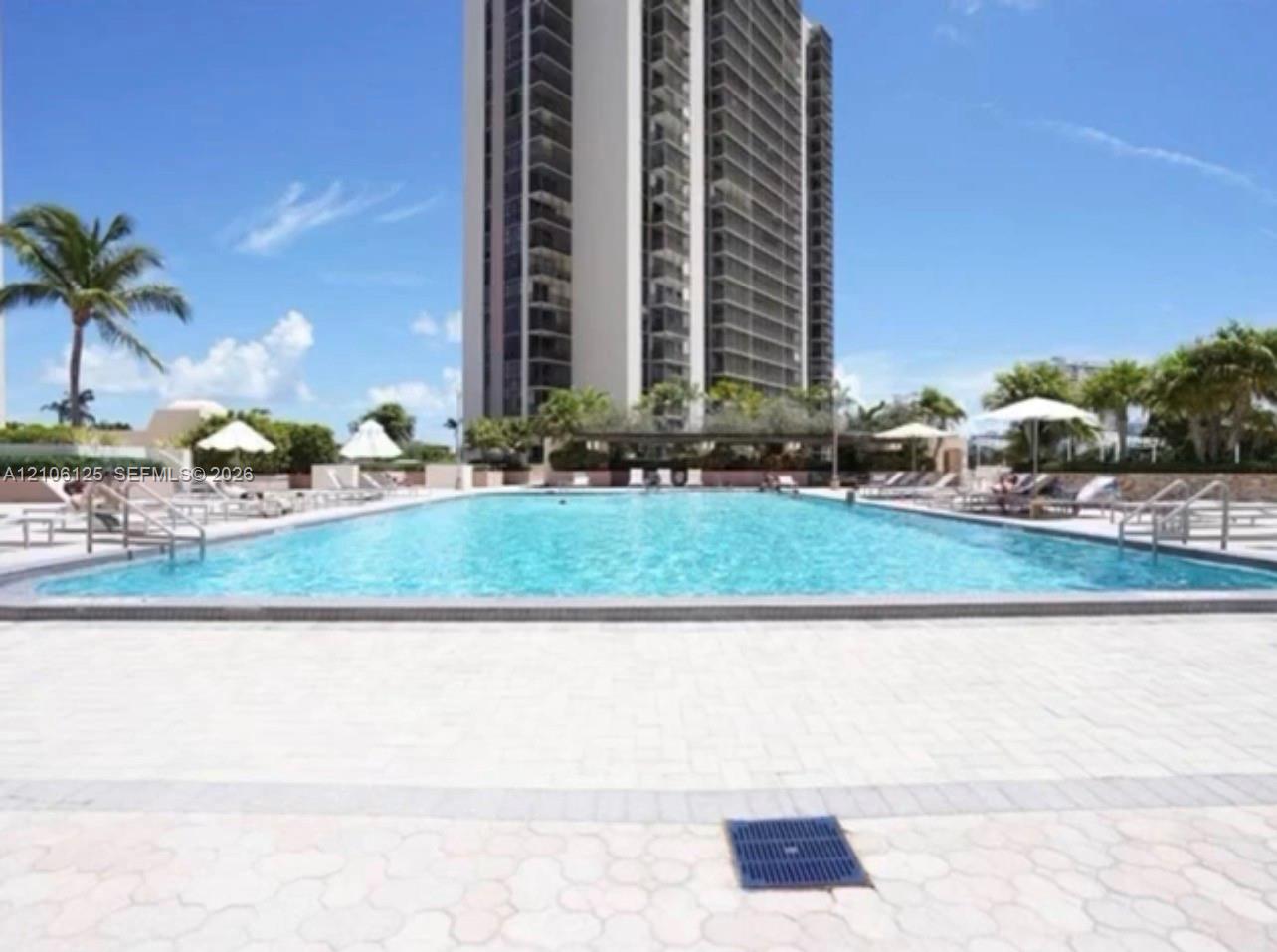 Large swimming pool with stone-paver decking, metal entry rails, and surrounding palm trees
