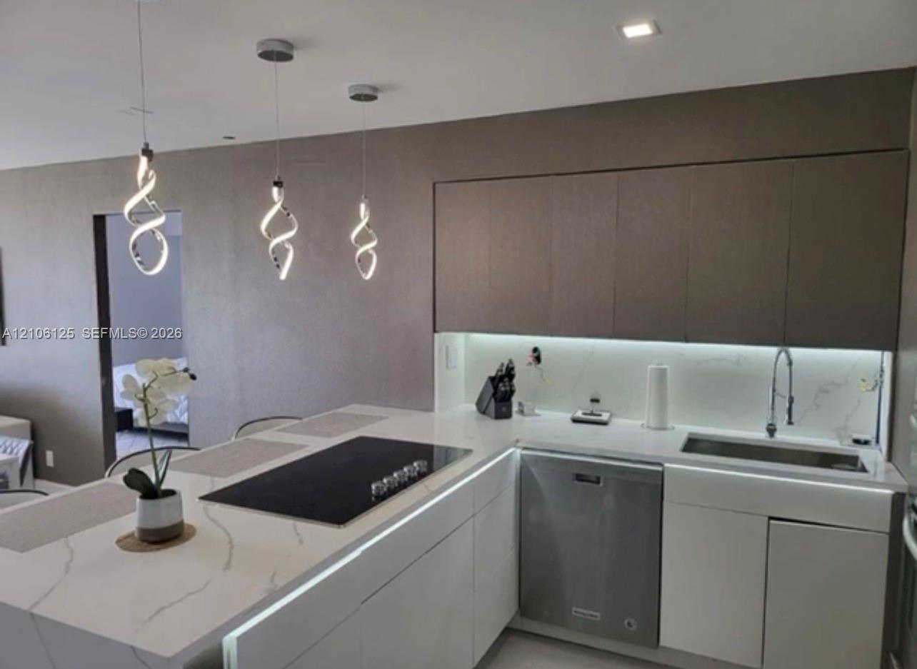 Kitchen featuring quartz countertops with integrated backsplash, flat-panel cabinetry, stainless steel dishwasher, inset cooktop, and three spiral pendant lights
