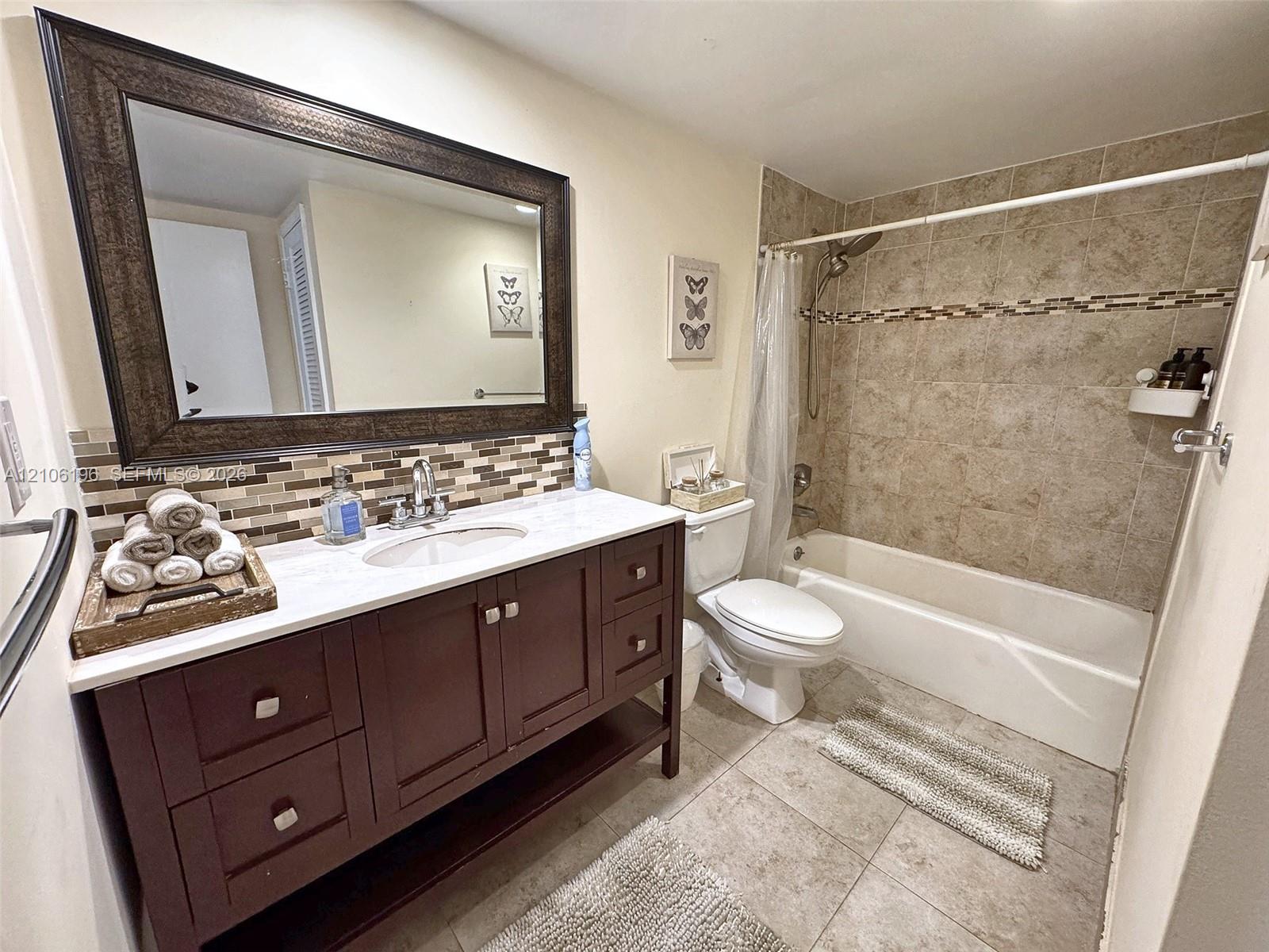 Bathroom featuring a dark wood-finish vanity with a light-toned countertop, oval undermount sink, multi-tonal glass tile backsplash, and a large framed mirror