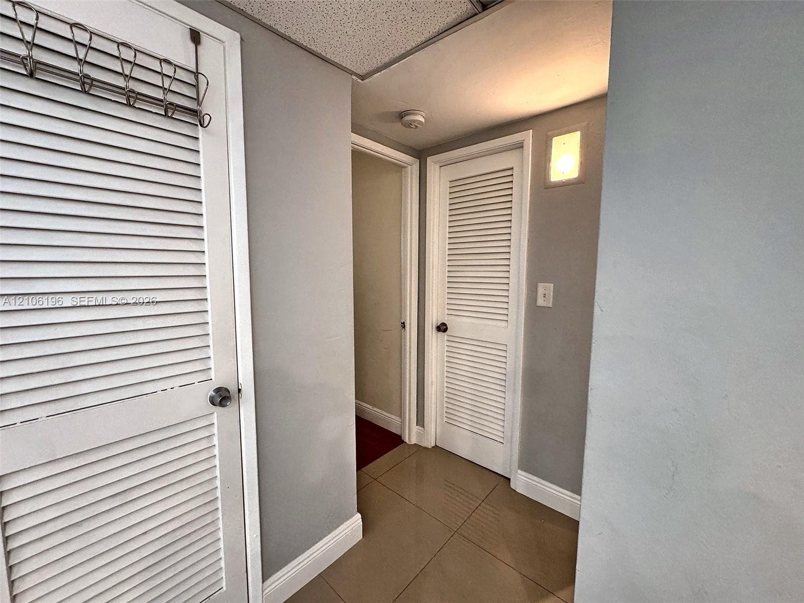Neutral-toned interior featuring large-format tile flooring, white louvered closet doors, and a wall-mounted sconce