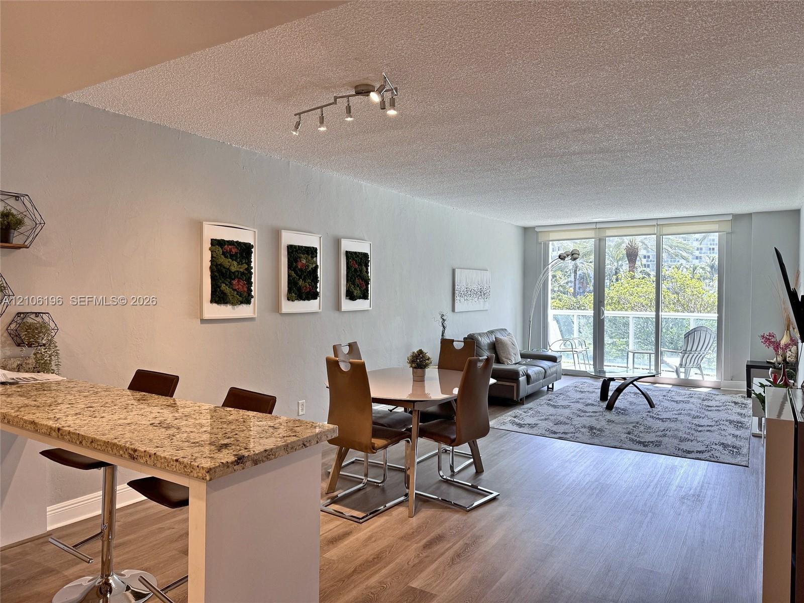 Open-concept living space featuring wood-finish flooring, a stone-surfaced breakfast bar, and multi-directional track lighting