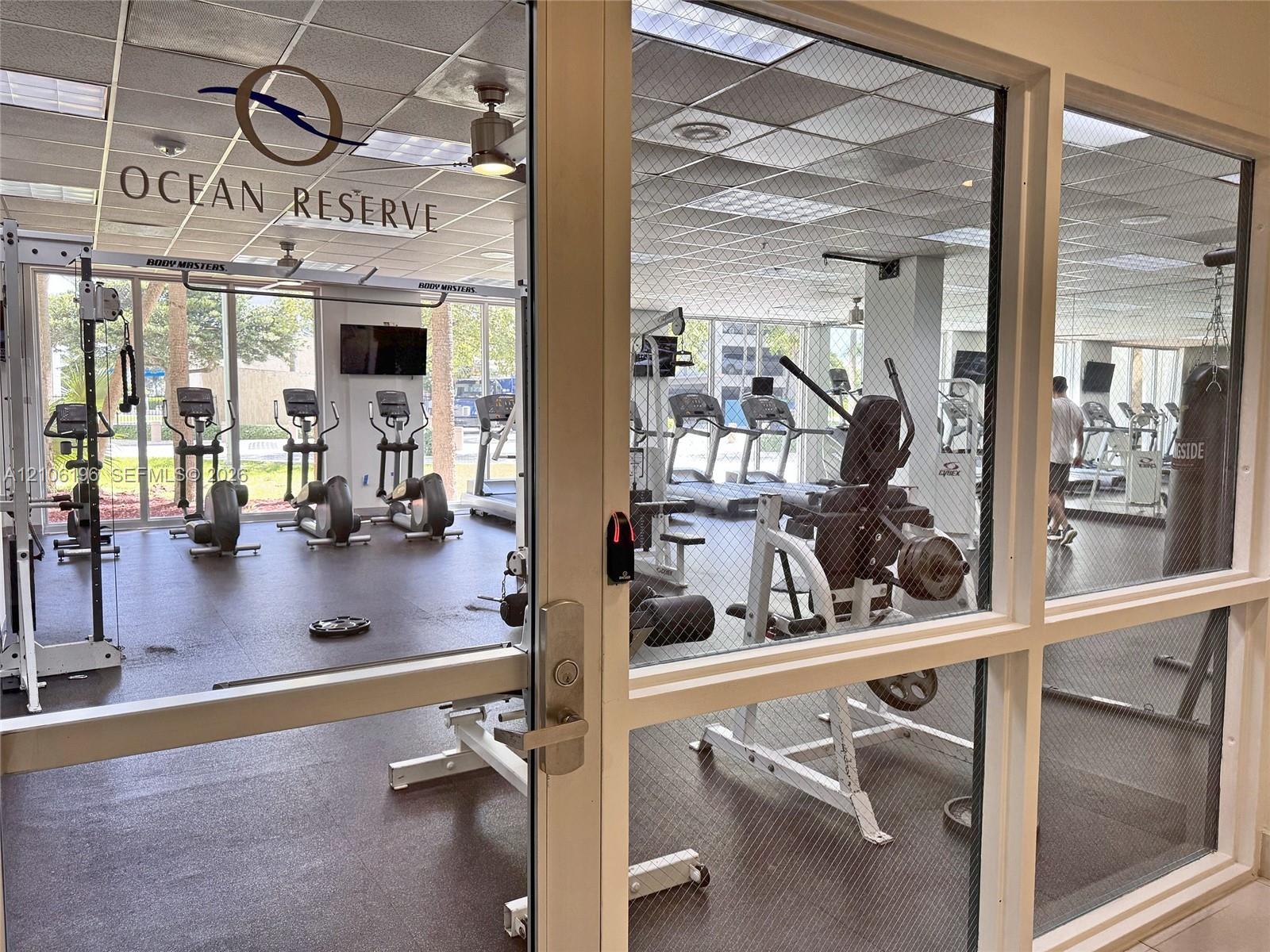 Fitness center featuring rubberized flooring, drop ceiling with recessed lighting, floor-to-ceiling windows, and fixed exercise equipment