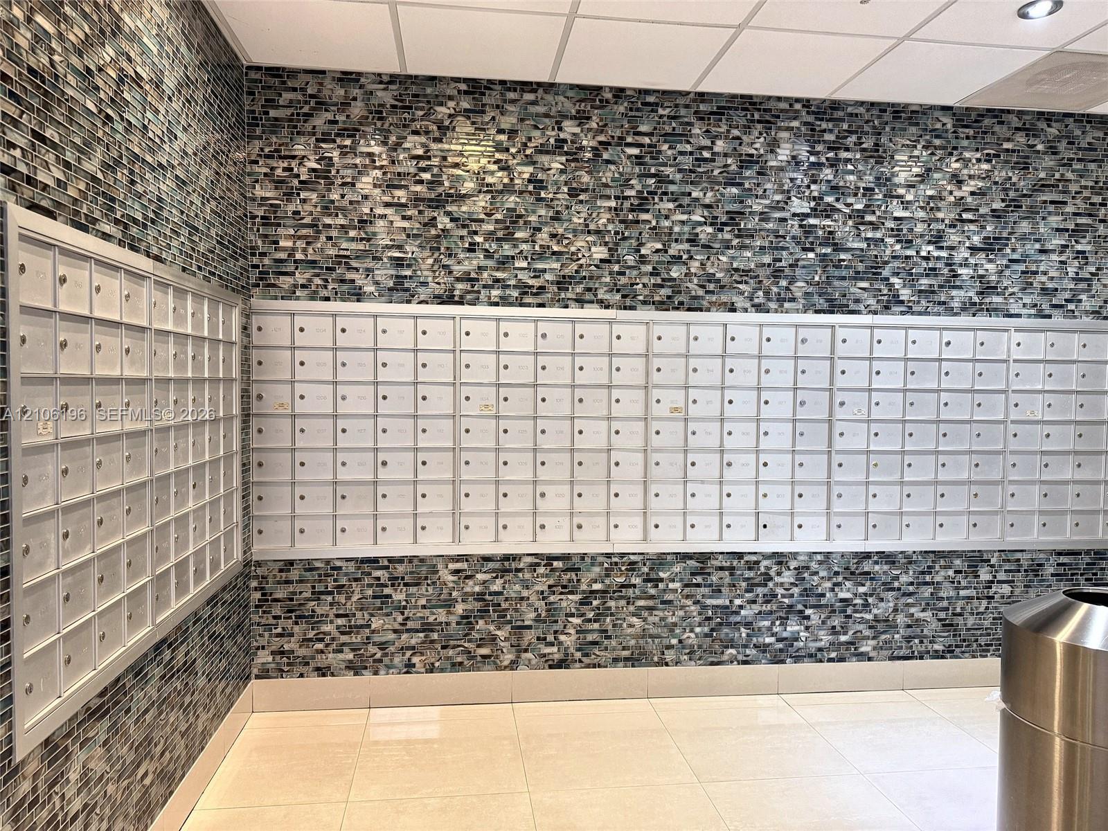 Common area featuring multi-unit metal parcel lockers, floor-to-ceiling glass-tile wall finishes, and polished tile flooring