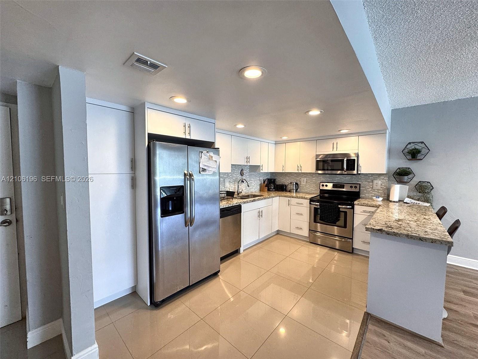 Kitchen featuring white shaker-style cabinetry, stone-finish countertops, stainless steel appliances, a mosaic tile backsplash, and ceramic tile flooring