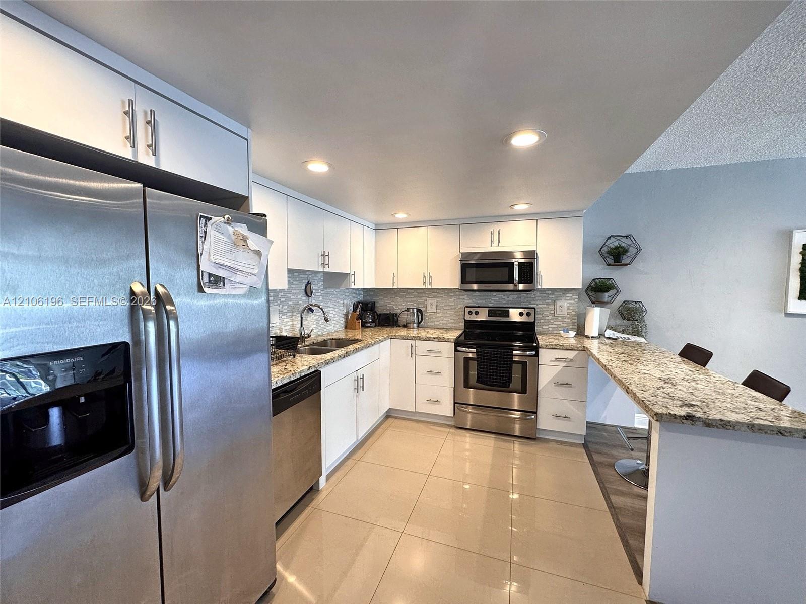 Kitchen featuring white cabinetry, stone-surface countertops, stainless steel appliances, a breakfast bar, and tile flooring