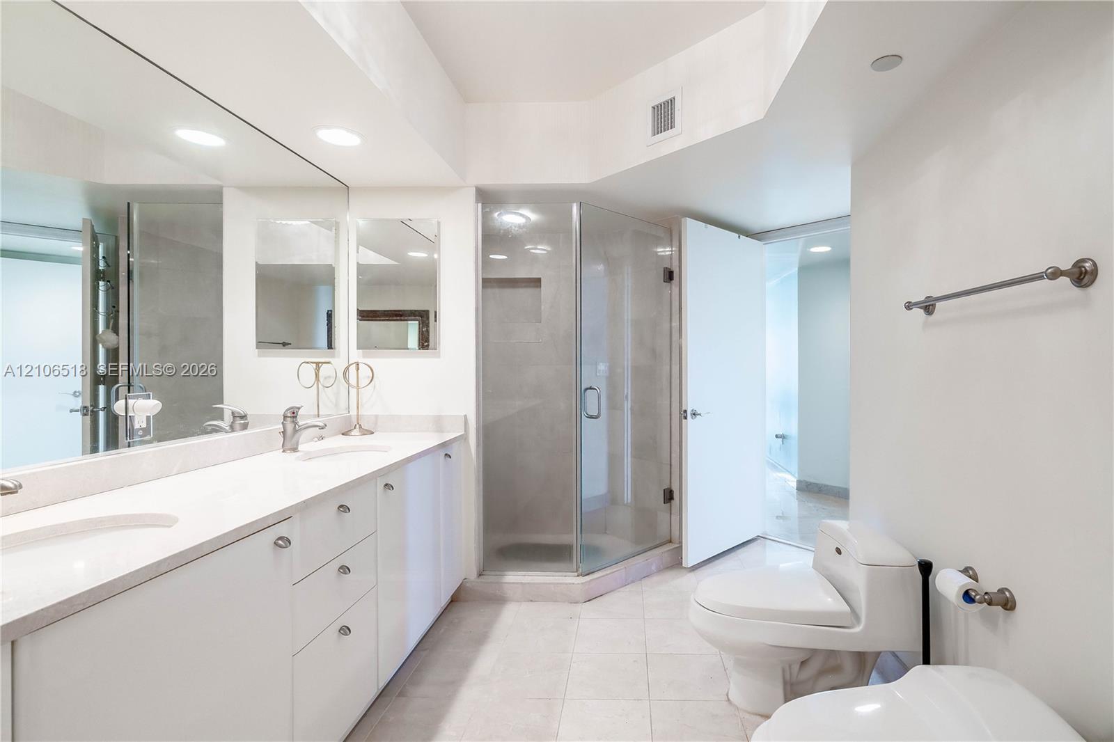 Double vanity with white cabinetry and solid-surface countertop, full-width wall mirror, glass-enclosed corner shower with tiled interior, and ceramic tile flooring