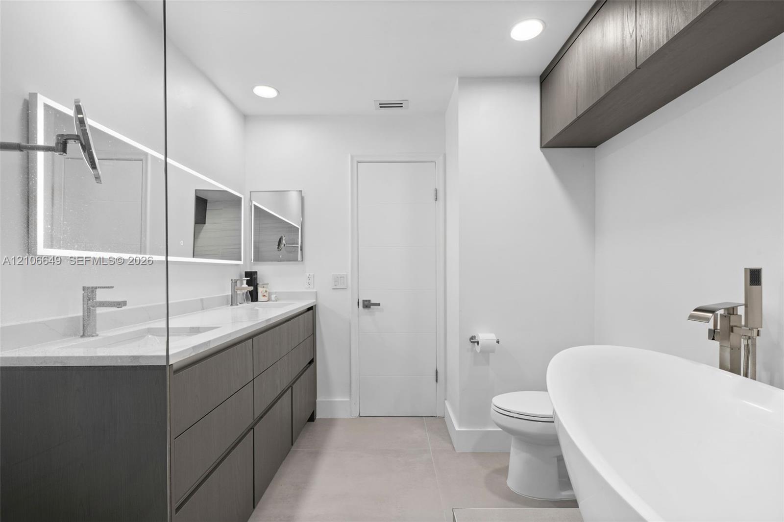 Modern dual vanity with stone countertop, freestanding soaking tub, wall-mounted faucets, and dark wood-finish cabinetry