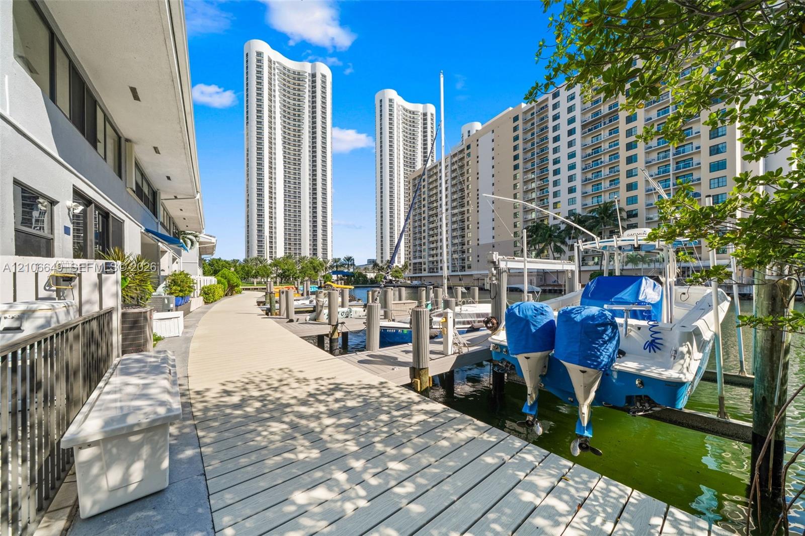 Waterfront exterior featuring a multi-level composite boat dock, stone-surfaced patio area, retractable blue awning, and large-format sliding glass doors