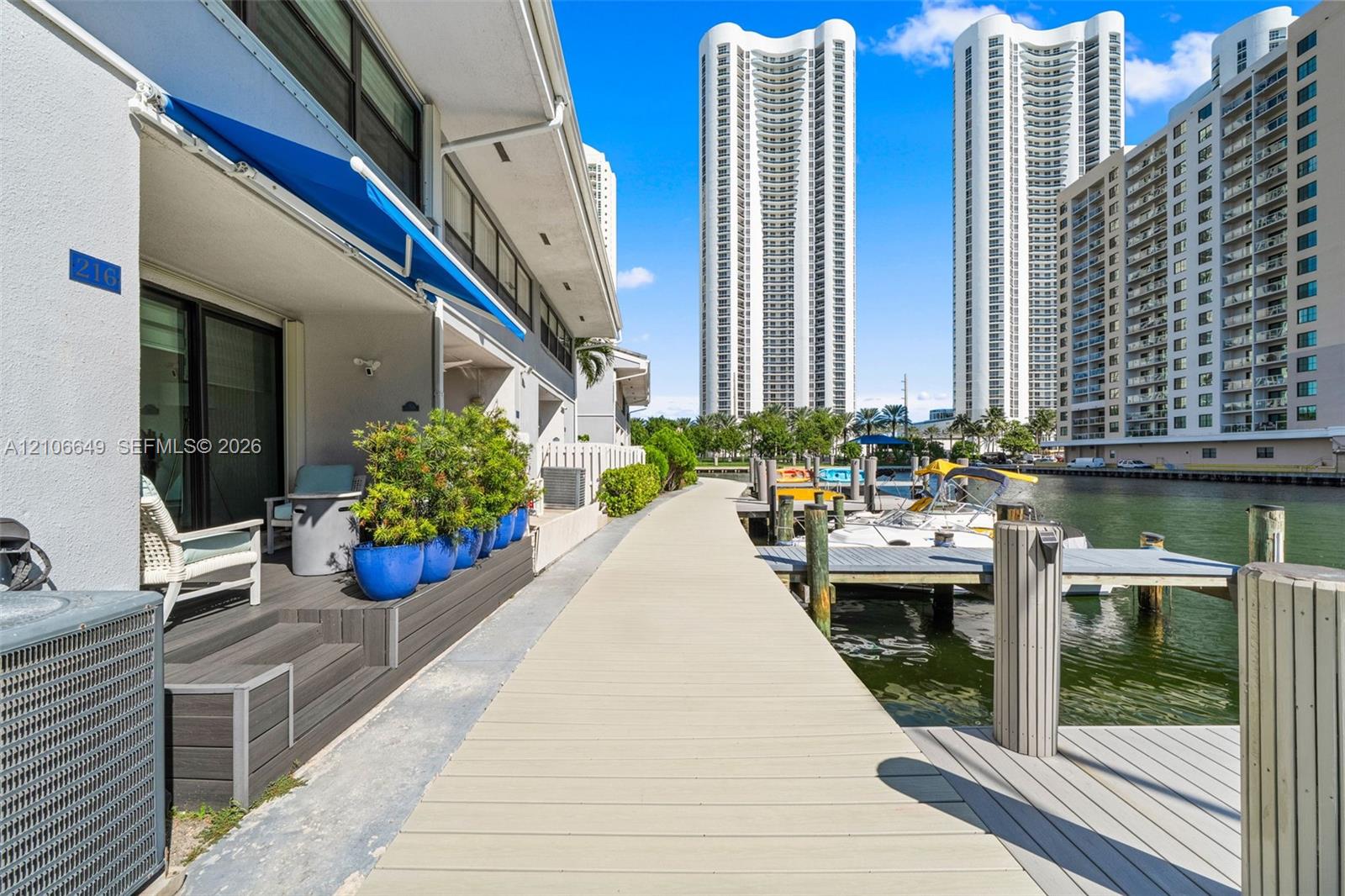 Covered balcony featuring wood-finish composite decking, a retractable fabric awning, and integrated wall-mounted lighting