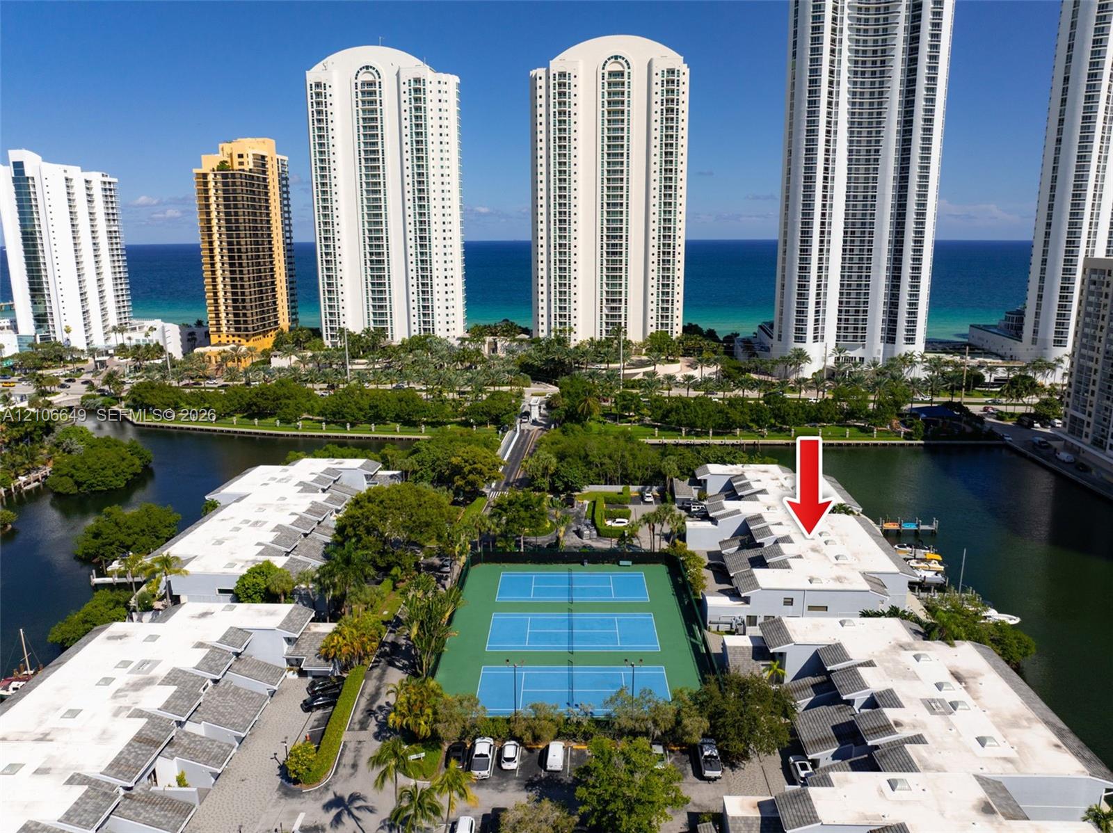 Waterfront residential complex featuring private boat slips, hardscaped docks, a multi-court tennis facility, and expansive coastal surroundings