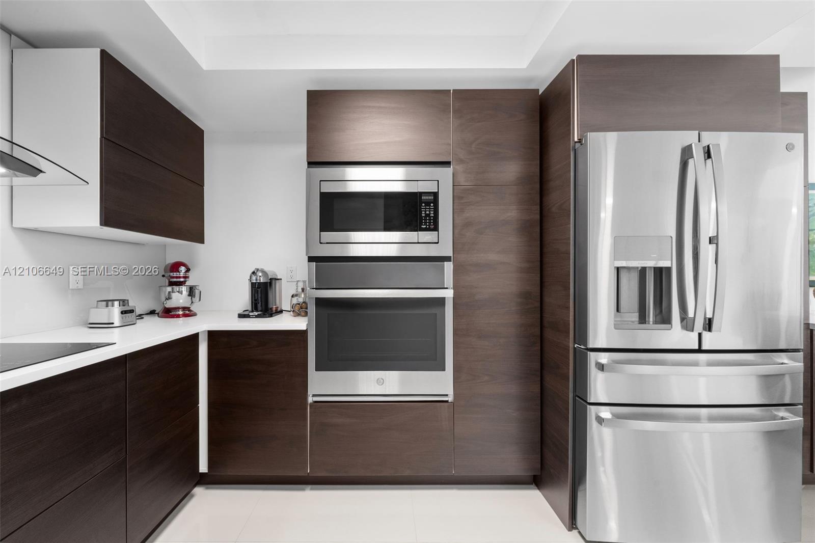 Modern kitchen featuring dark wood-finish cabinetry, solid surface countertops, stainless steel wall oven, built-in microwave, and stainless steel french-door refrigerator
