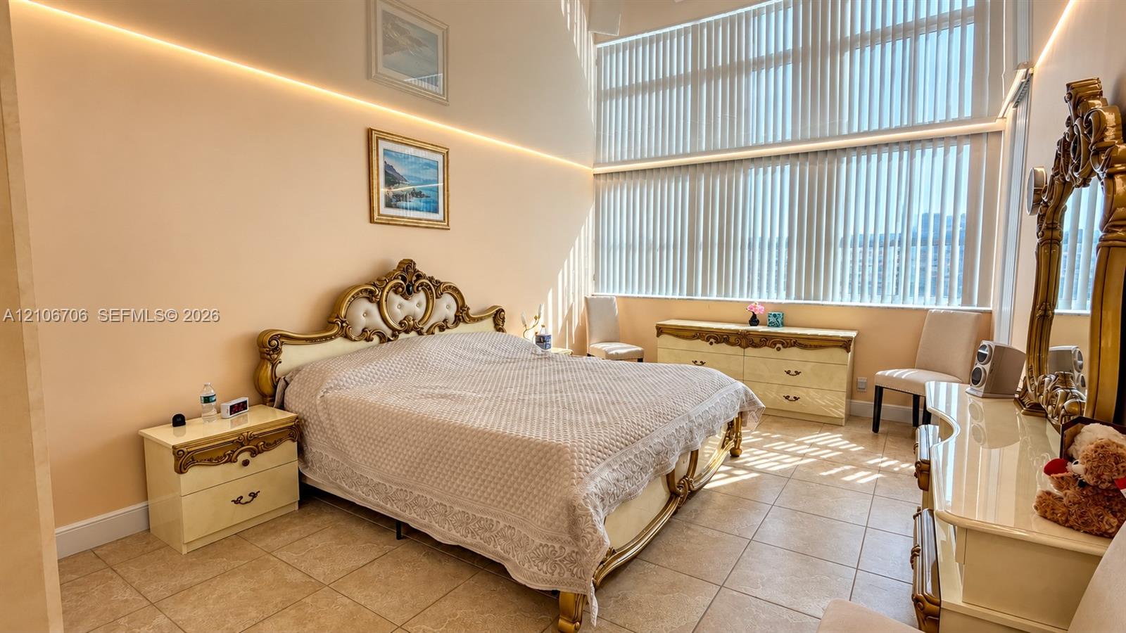 High ceilings featuring integrated cove lighting, large-format tile flooring, and expansive windows with vertical blinds