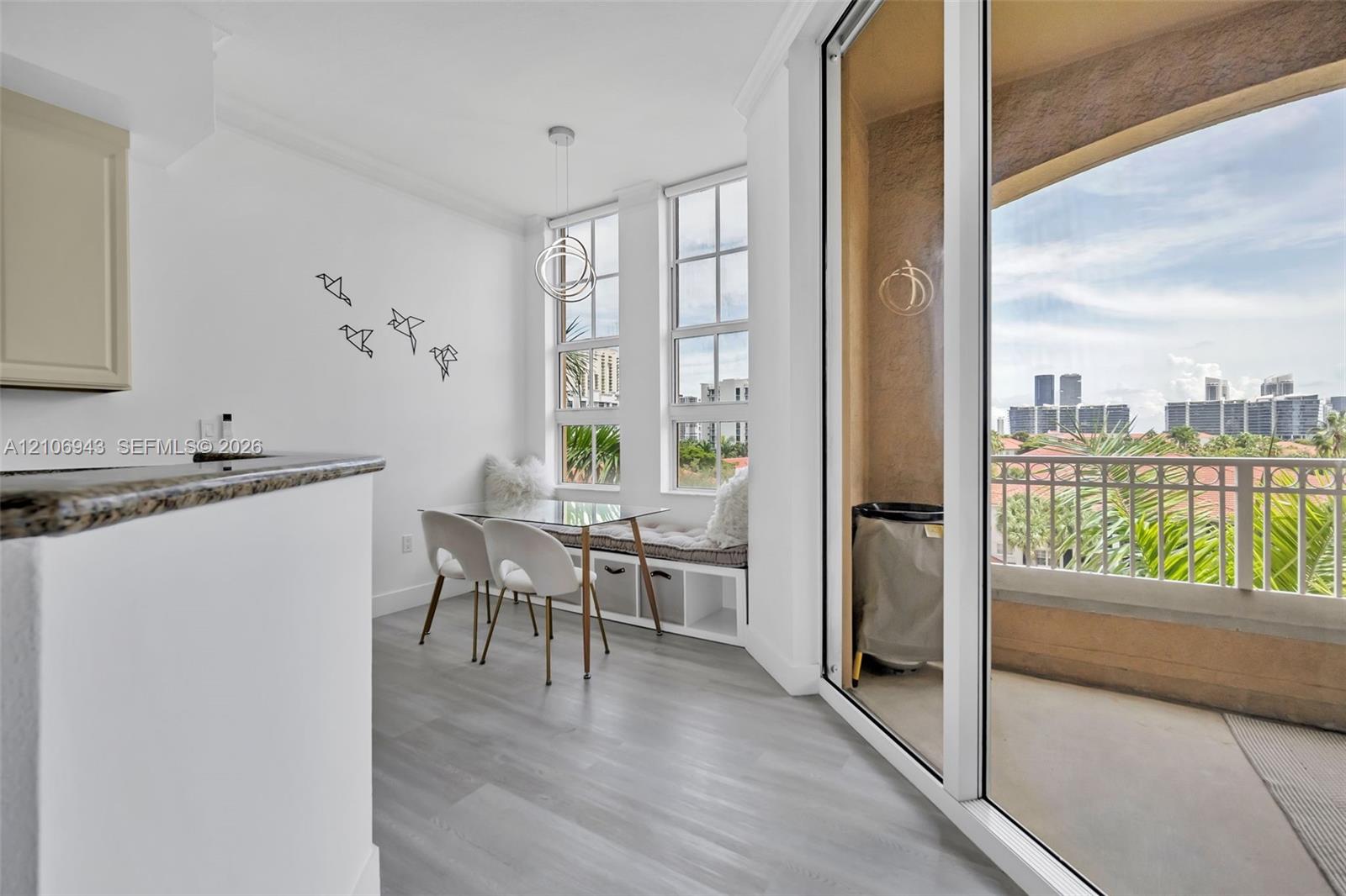 Dining area featuring wood-finish flooring, built-in window seating with integrated storage, large multi-pane windows, a contemporary circular pendant light, and sliding glass doors opening to a covered balcony