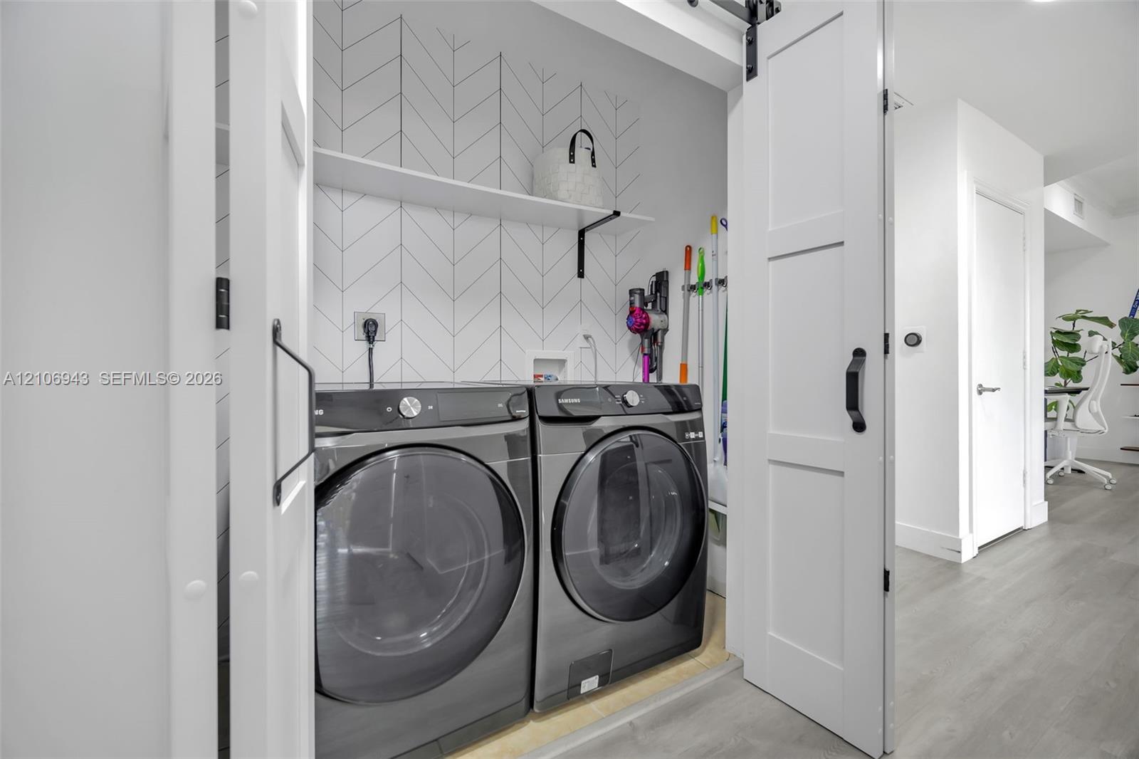 Laundry area featuring a sliding barn door, herringbone-patterned tile backsplash, and built-in shelving