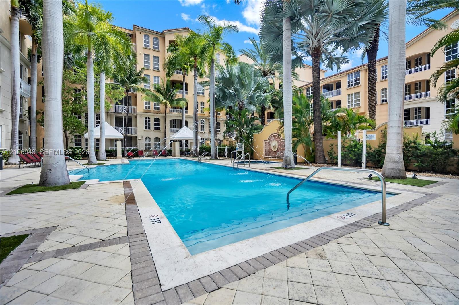 Outdoor swimming pool featuring a stone-paver deck, built-in water fountains, and mature palm trees