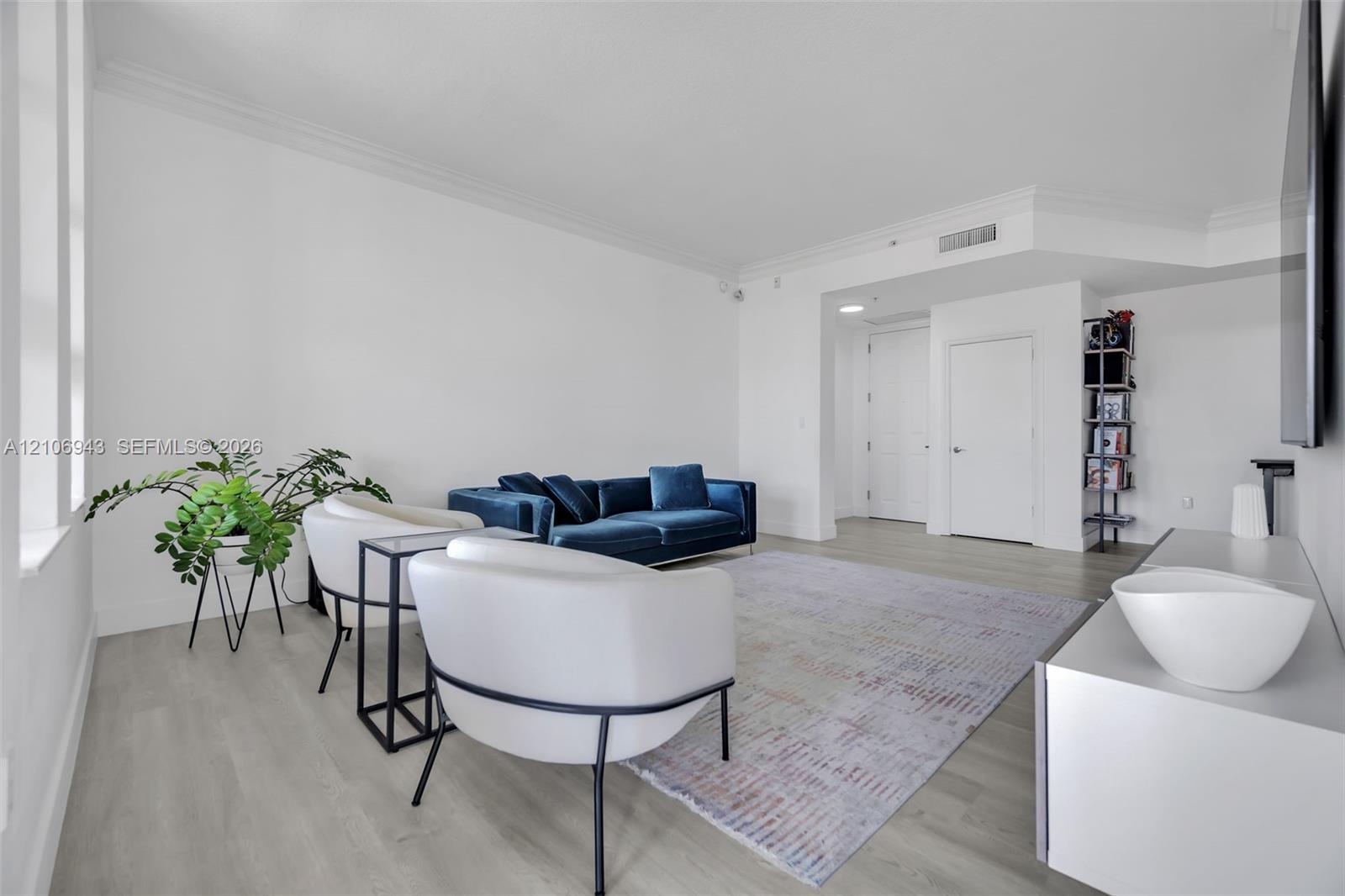 Open-concept living space featuring wood-finish flooring, crisp neutral wall paint, crown molding, and tall vertical windows