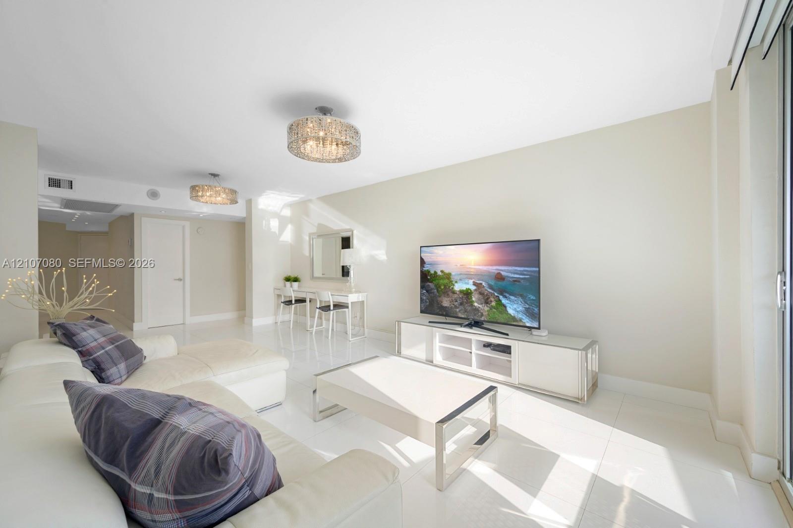Open-concept living space featuring high-gloss tile flooring, dual contemporary drum-style pendant light fixtures, and sliding glass doors