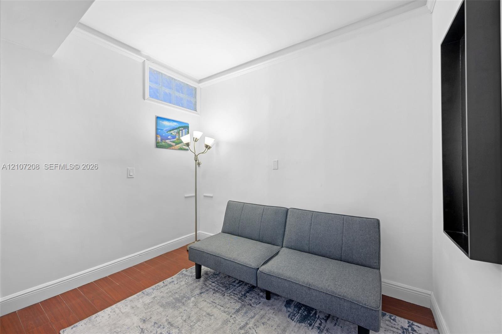 Interior space featuring wood-finish flooring, crown molding, a high-set glass block window, and a recessed wall niche with a matte black frame