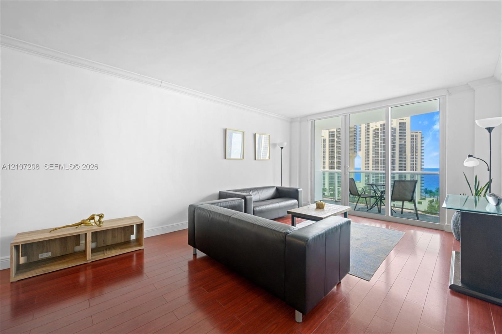 Living area featuring wood-finish flooring, crown molding, and floor-to-ceiling glass sliding doors opening to a balcony