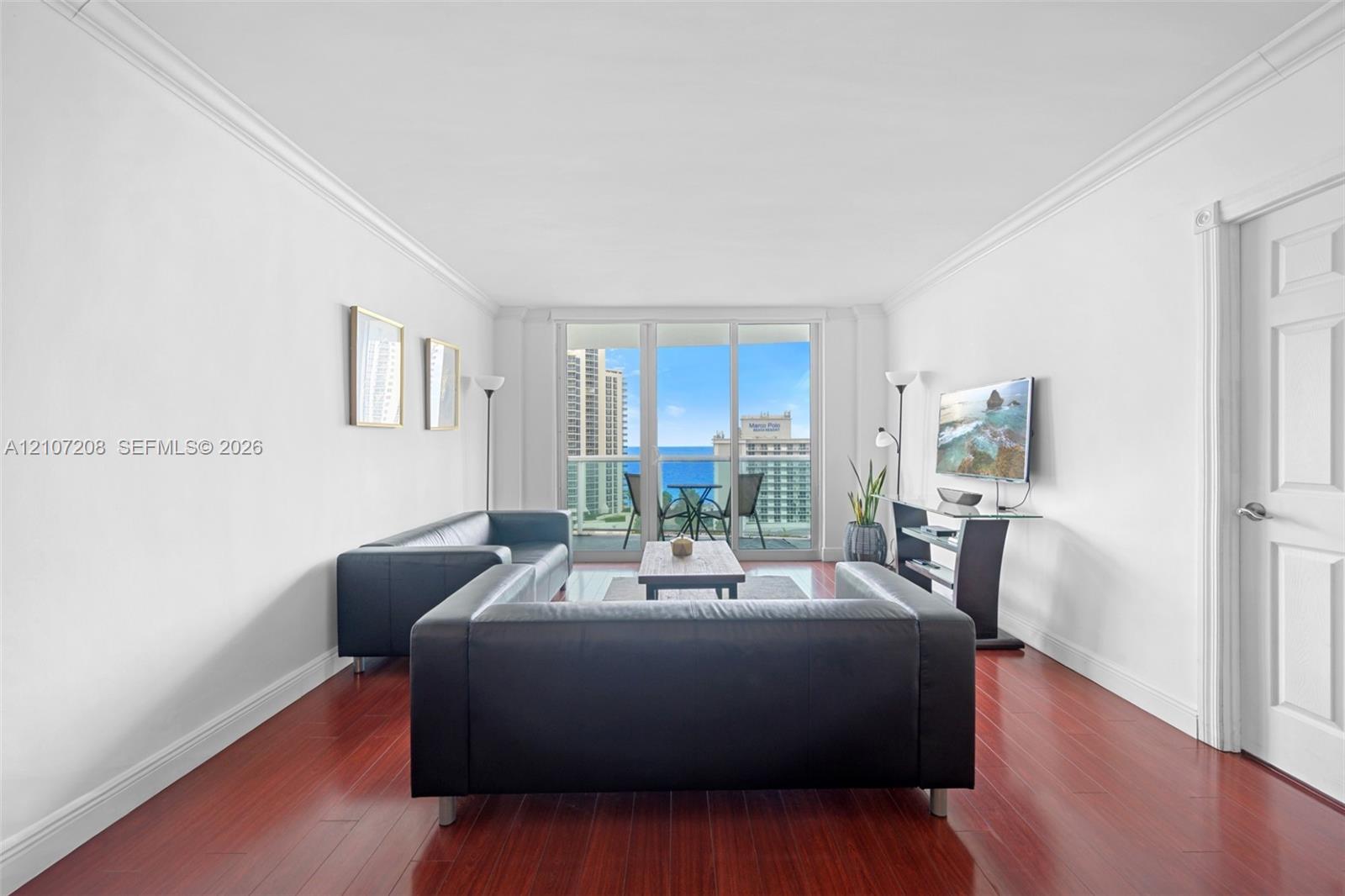 Interior space featuring wood-finish flooring, crown molding, and floor-to-ceiling glass panel sliding doors opening to an exterior balcony