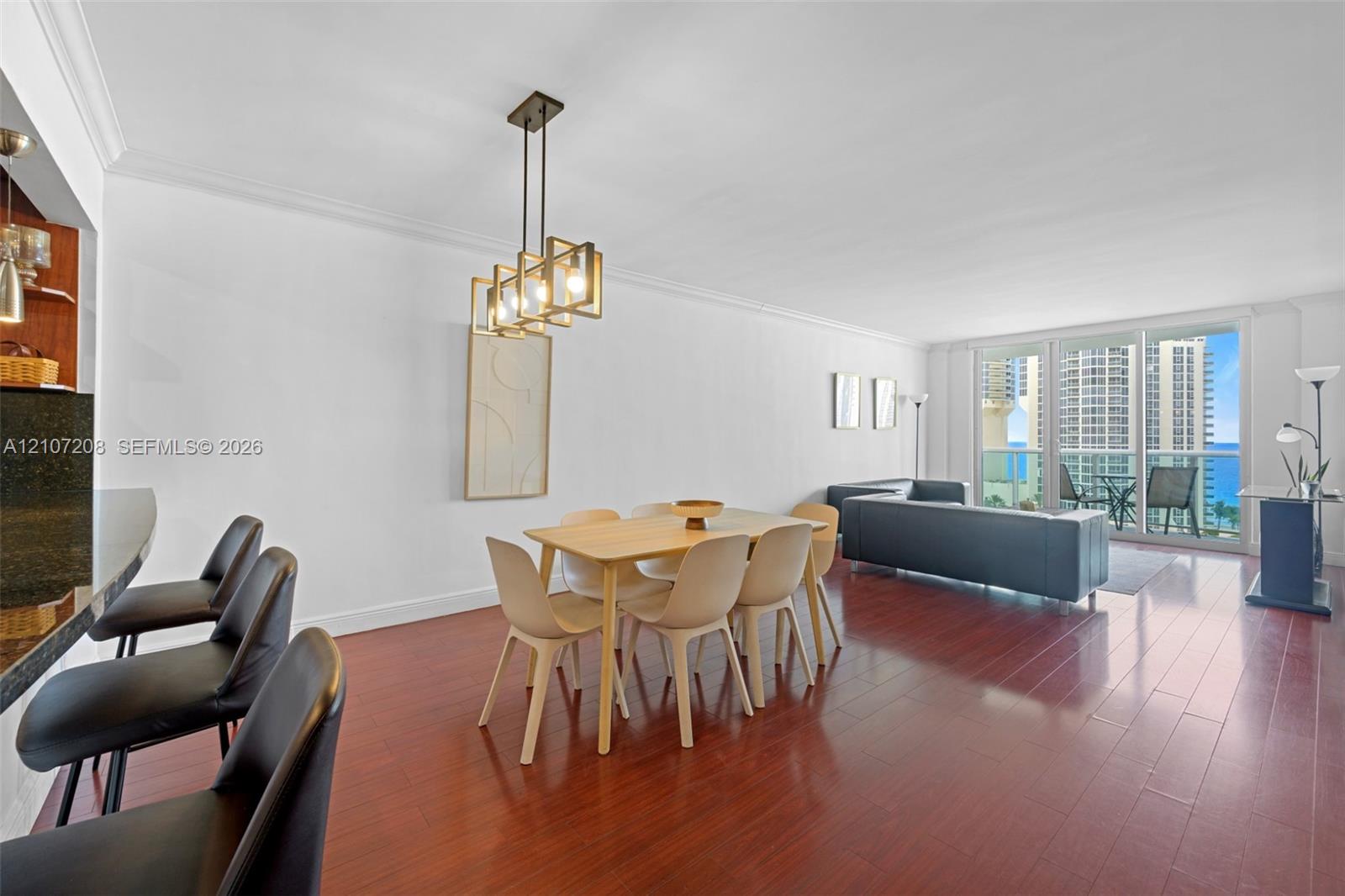 Open-concept interior featuring wood-finish flooring, a kitchen breakfast bar with stone-finish countertop, geometric pendant lighting, and large sliding glass doors providing outdoor access