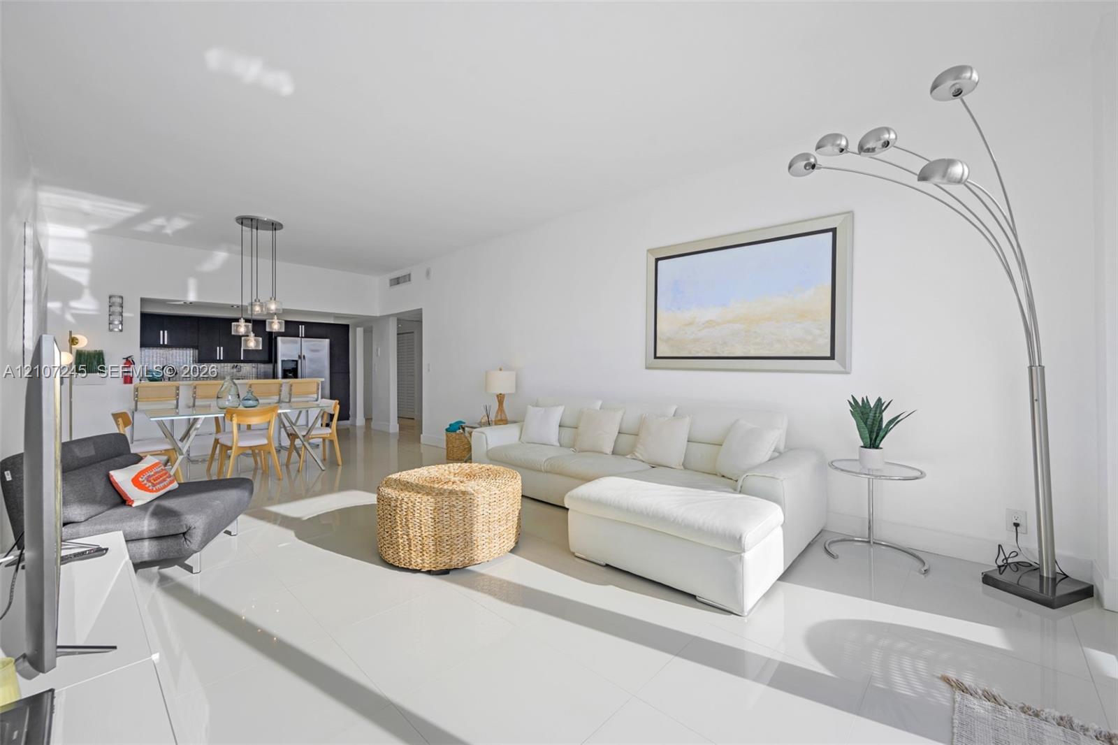 Open-concept interior featuring large-format tile flooring, recessed ceiling lighting, and a kitchen equipped with dark cabinetry, integrated bar seating, and multi-pendant lighting