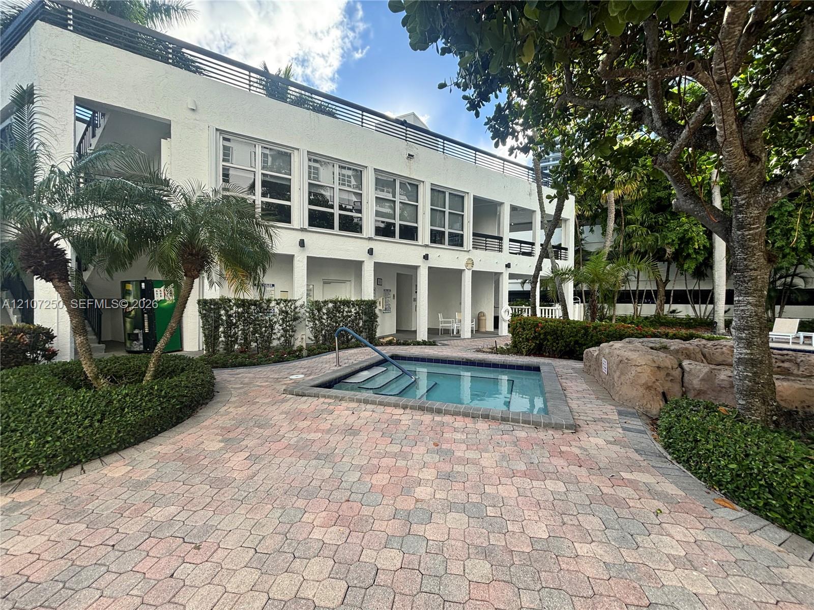 In-ground spa featuring a stone-lined border, surrounded by decorative paver patio, integrated landscaping, and a multi-level structure with balcony railings