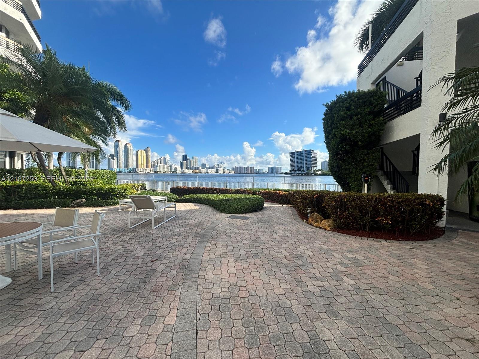 Paver patio featuring manicured hedging, established palm trees, and waterfront exposure