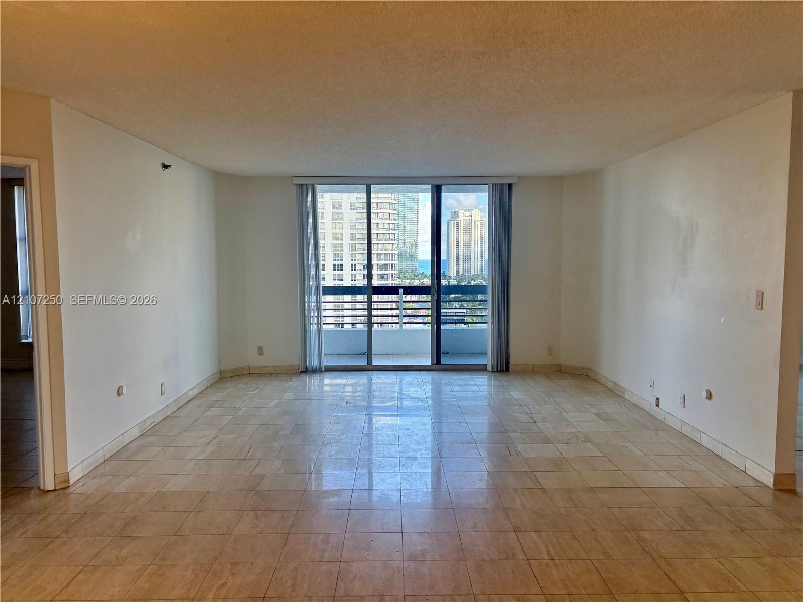 Large living area featuring stone tile flooring and floor-to-ceiling sliding glass doors opening to a balcony