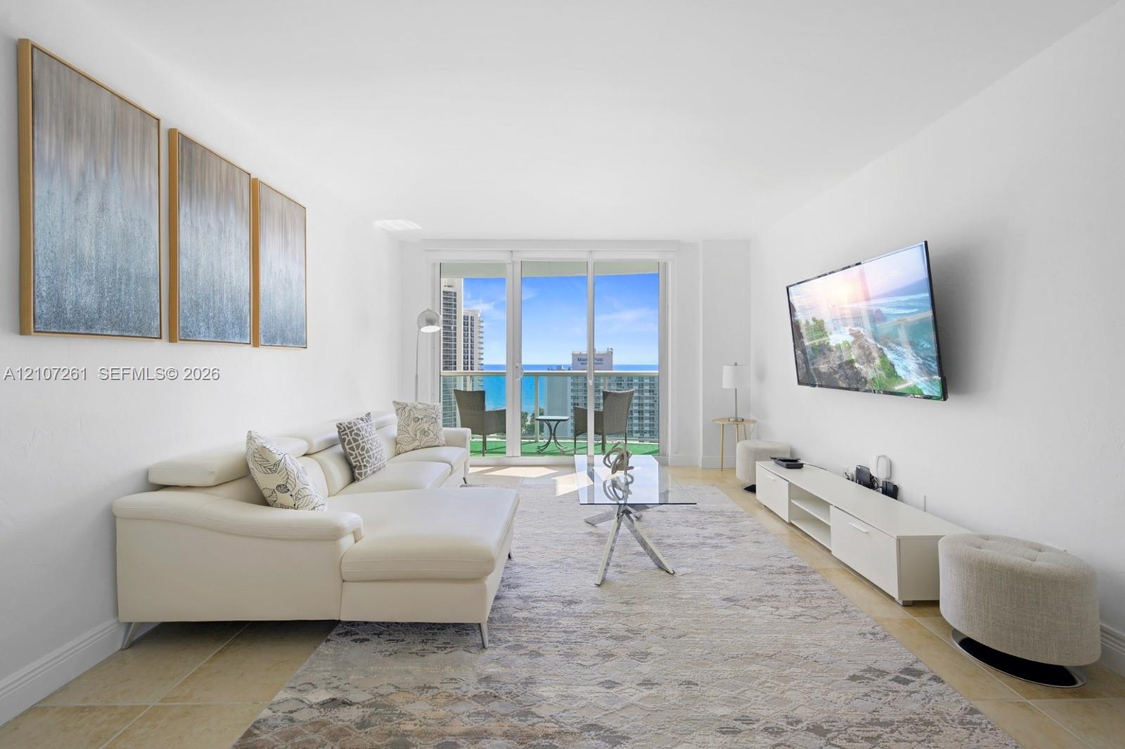 Living area featuring large-format tile flooring, expansive floor-to-ceiling glass sliding doors, and a private balcony