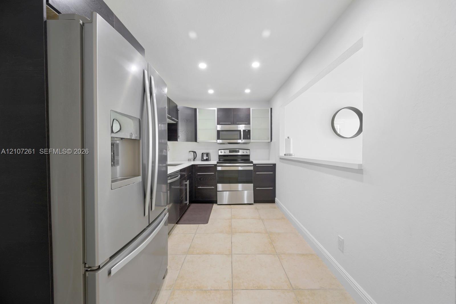 Kitchen featuring dark cabinetry, stainless steel appliances, recessed ceiling lighting, and tile flooring