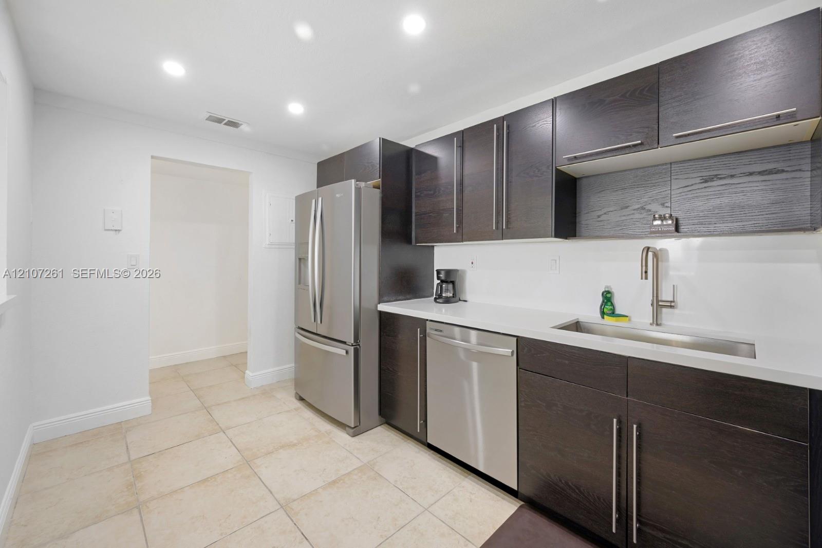 Kitchen featuring dark wood-finish cabinetry, white solid-surface countertops, recessed ceiling lighting, stainless steel appliances, and tile flooring